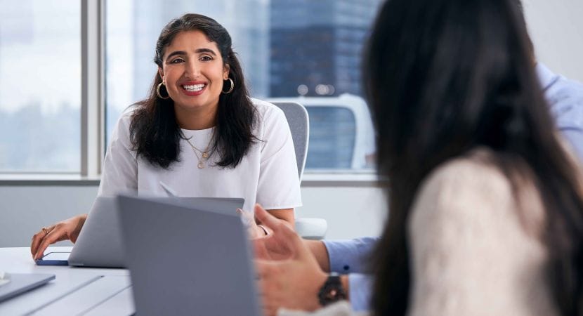 A smiling woman speaks to another woman in a conference room