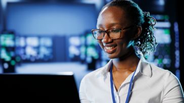 An IT professional smiles at a computer monitor.
