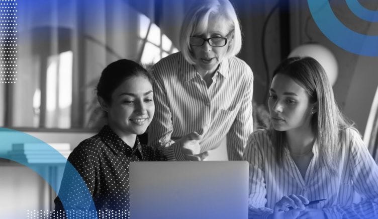 An older woman points something out on a computer screen to two younger women seated in front of her. /women-tech/5-advice-effective-stem-mentor