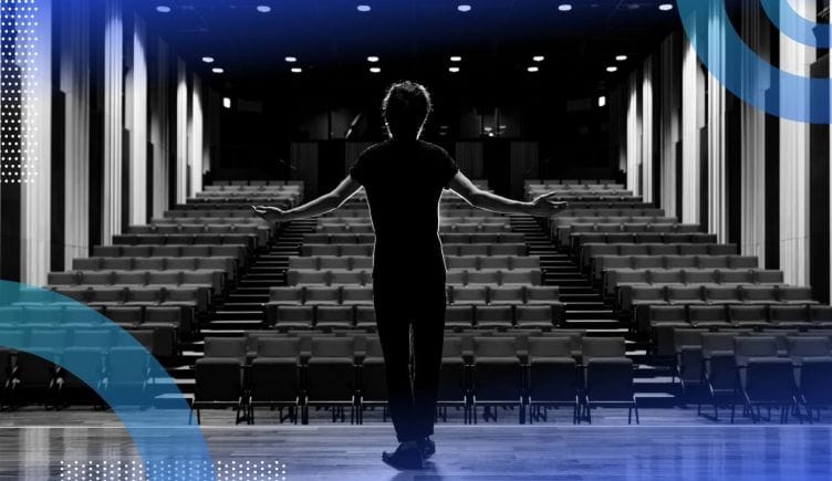 A performer stands onstage in front of an empty theatre