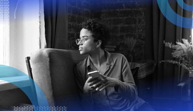 A Black woman gazes pensively out a window, her phone forgotten in her hands. /wearables/daydreaming-augmented-reality