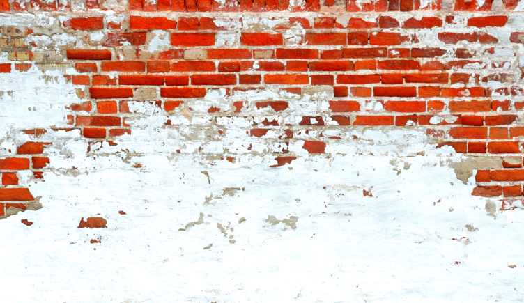 A brick wall whose white paint is slowly chipping away to reveal colorful brick underneath.