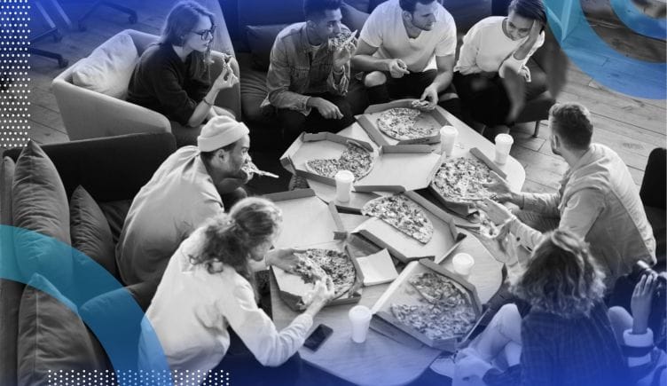 A group of people gather around a table covered with different pizzas. /remote-work/make-remote-work-more-fun