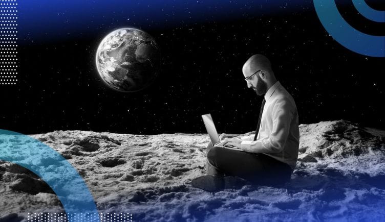 A man works on a laptop on the moon with the earth in the background