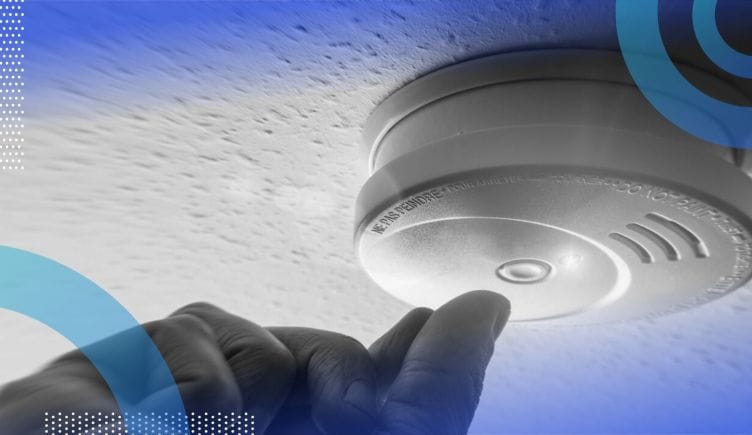 A hand pushes the button on a ceiling smoke detector