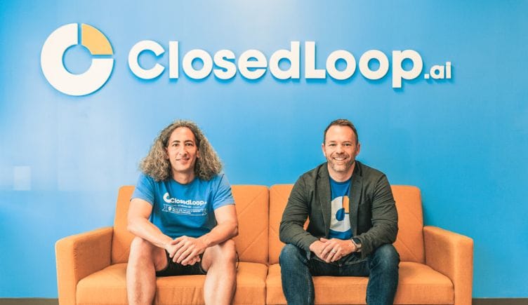 Closedloop team members sitting on a couch with the Closedloop logo on the wall behind them