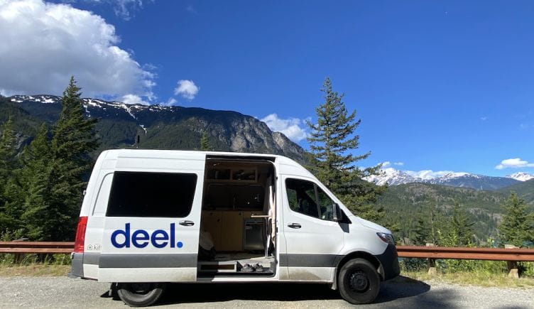 A white van with the blue Deel logo parked in front of a mountain.