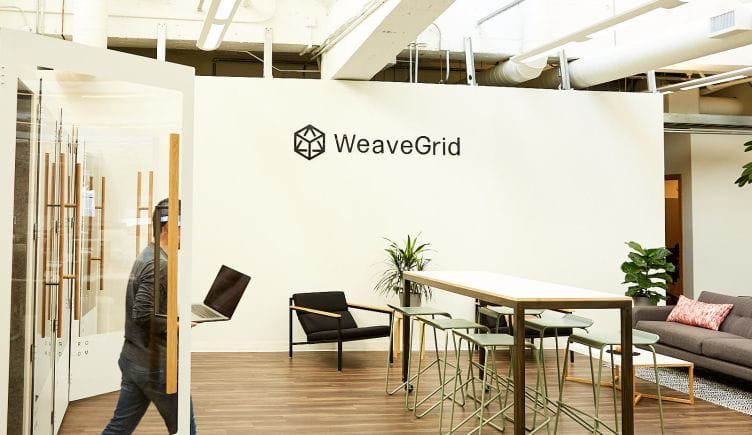 weavegrid's office with its logo on white walls and an open workspace. a man carrying a laptop. 
