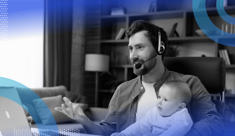 A bearded man wears a headset and holds a baby while talking into a computer. /remote-work/4-lessons-remote-working-parent