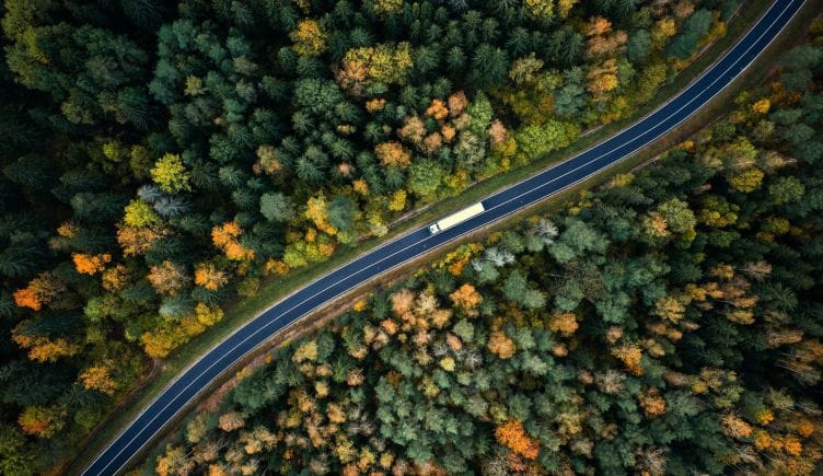 A truck travels an empty, winding highway during early fall colors.
