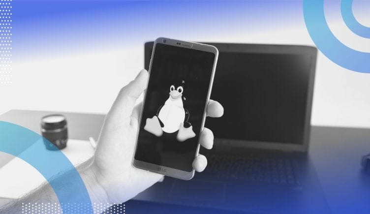 A hand holds a smartphone with the Linux logo in front of a laptop