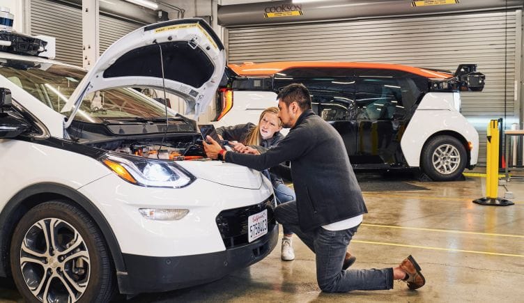 Two Cruise workers look under the hood of a vehicle in Cruise's garage