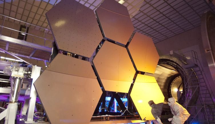 A scientist looking over several large, hexagonal panels of metal in a lab.