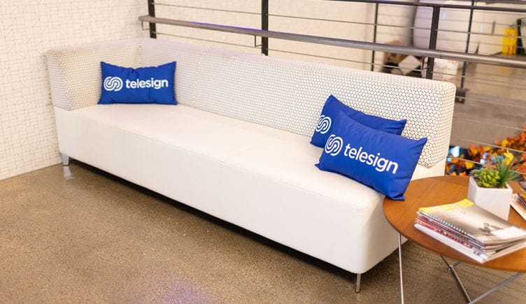 A white couch with several Telesign pillows on it.