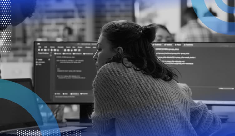 Python algorithms image of a woman shot from behind. She looks intently at two computer screens in front of her that are full of code. 