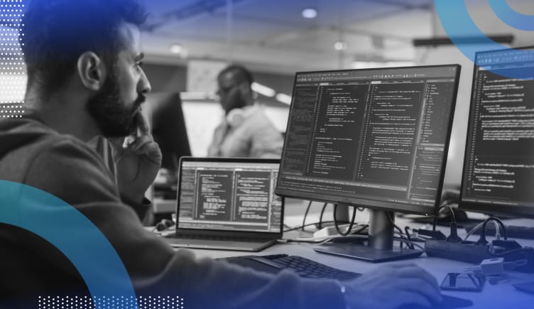 Image of a bearded man looking intently at three monitors with code on them.