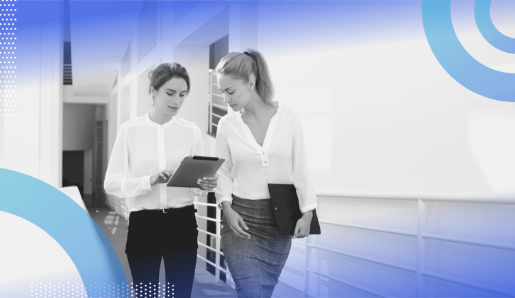 HRBP image of two women walking down a corridor. One holds an iPad and points to something on the screen, the other looks over her shoulder.