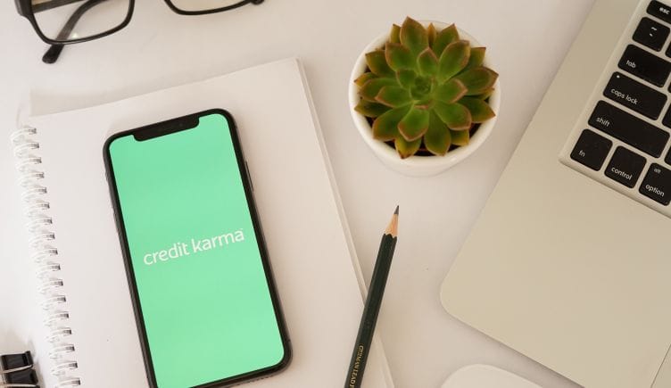 A phone shows Credit Karma's logo next to a laptop and succulent