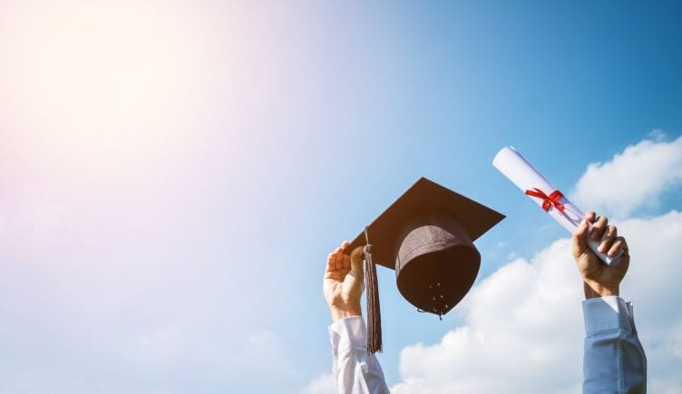 person holding up graduation cap and diploma under sunshine