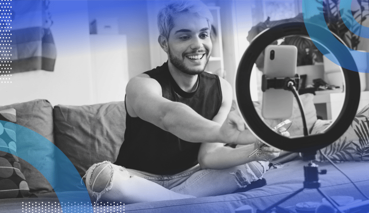 influencer marketing image of a person with bleach blonde hair and torn jeans sitting cross-legged on a couch. They reach forward to hit record on their smartphone, which sits inside a ring light.