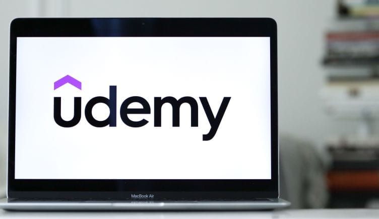 Udemy's logo on a laptop, resting on a gleaming desk.