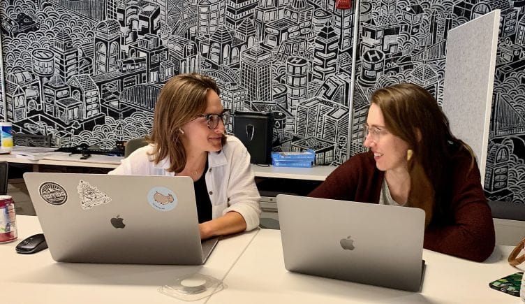 Two Cohere team members talking, smiling with laptops open