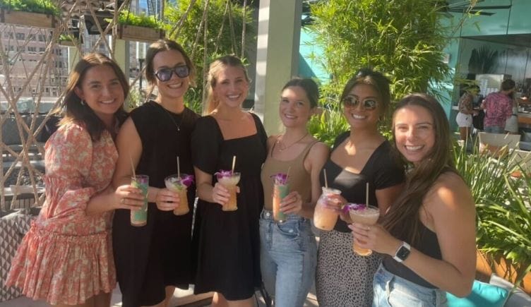  Six Navan employees — all women — with tropical drinks in hand pose for group photo