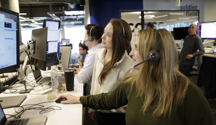Employees at trade desk with headsets on, looking at screen