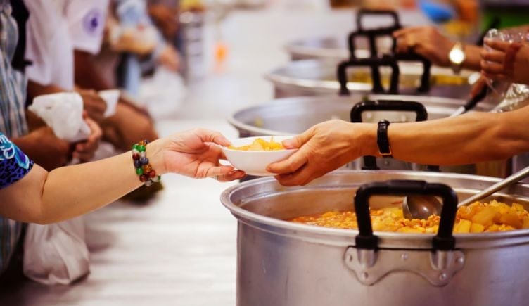 Volunteers spoon food into bowls and serve it to people.