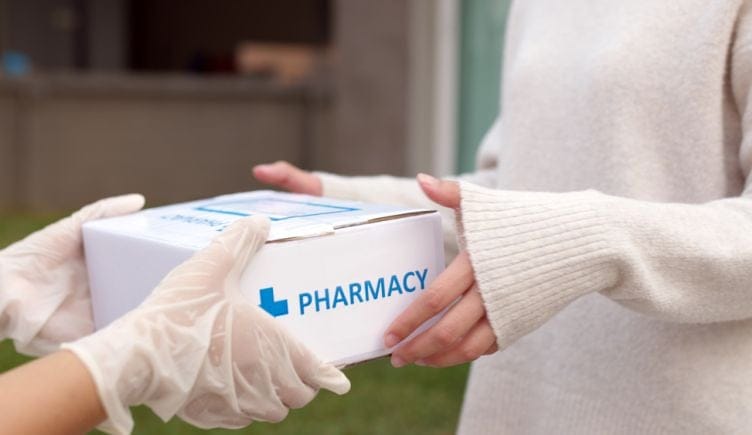 A delivery person hands a pharmacy package to a recipient.