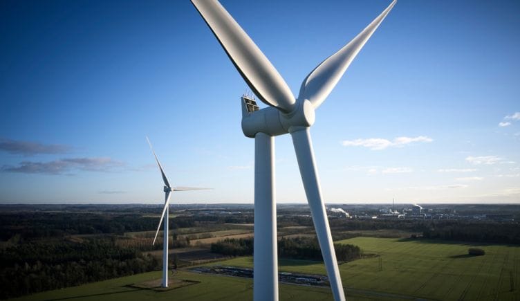 Two wind turbines stand tall in a field to capture energy from the wind.