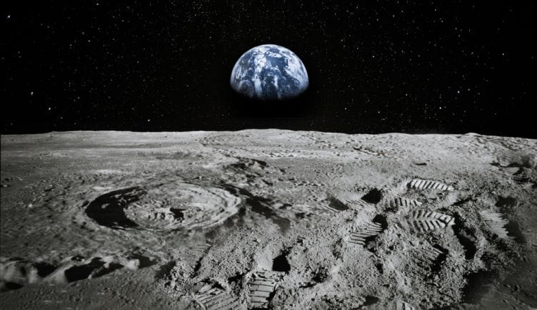 Footprints on the moon sit in the image foreground with a portion of Earth visible in the distance. 