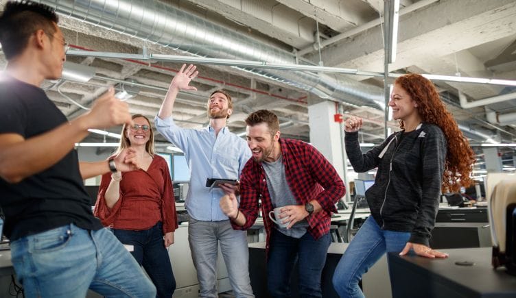 Candid photo of five team members celebrating in the office, industrial-style ceiling overhead.