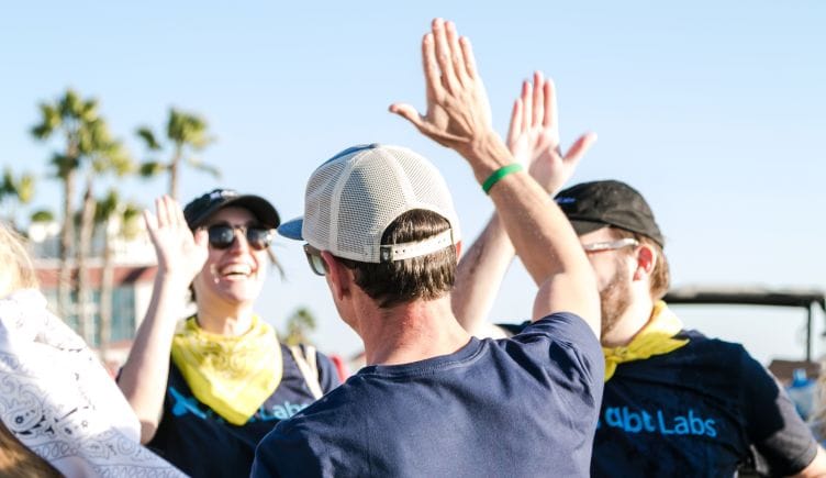 dbt Labs team members high-fiving outside with palm trees in the background.