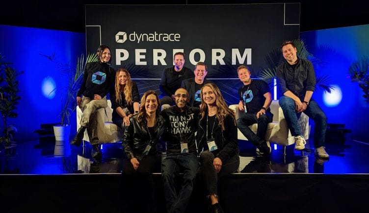 Nine Dynatrace team members sit on a stage with blue backlighting and a sign reading “Dynatrace Perform.”
