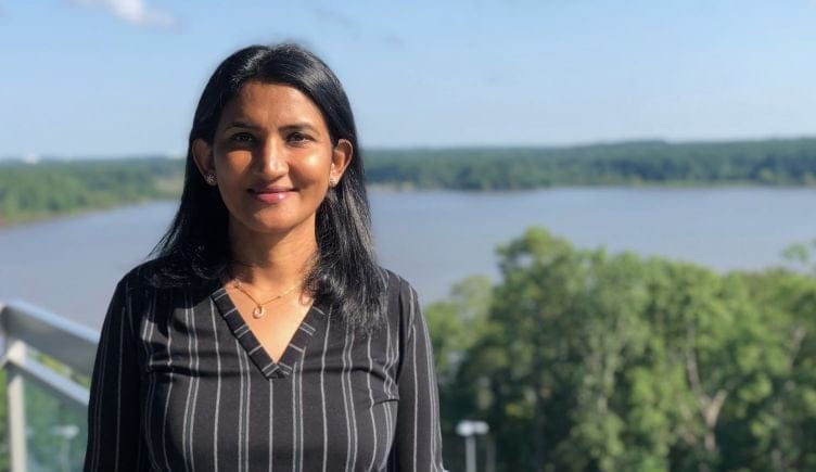 Portrait of Sushma Punuru on a balcony overlooking a lake with trees surrounding.