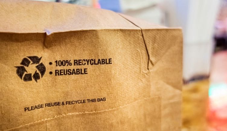 A close up of the bottom of a brown paper bag labeled recyclable and reusable to represent sustainability.