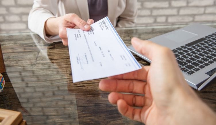 A close up of one hand passing a check to another hand over a desk to represent companies that pay well.
