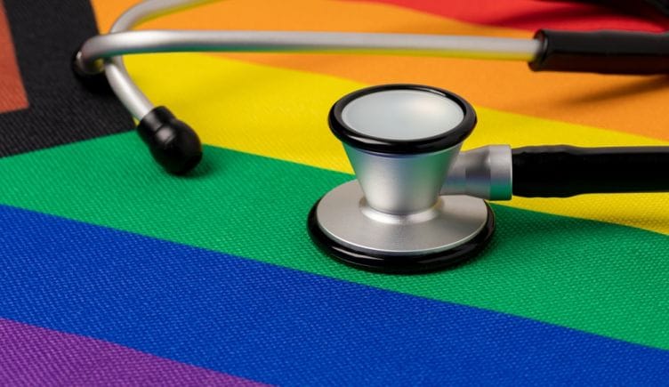 A doctor's stethoscope sits on top of the progress pride flag.