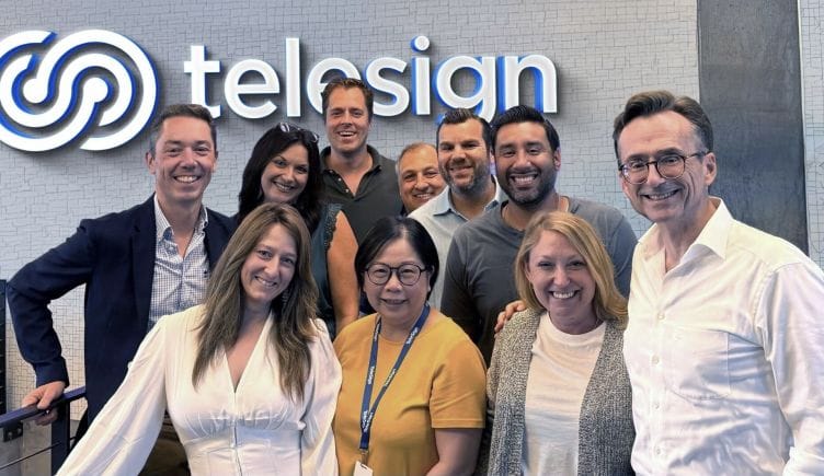A group of Telesign employees stand together in front of the company sign.