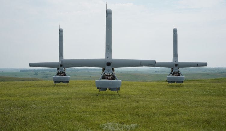 Three of Shield AI’s V-BAT drones sit in an open green field. 