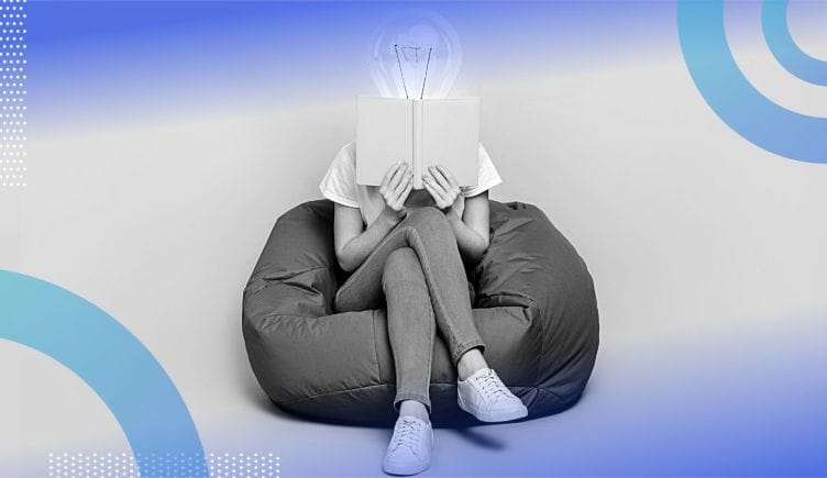 A person with a lightbulb for a head sitting cross-legged on a beanbag chair reading a book.