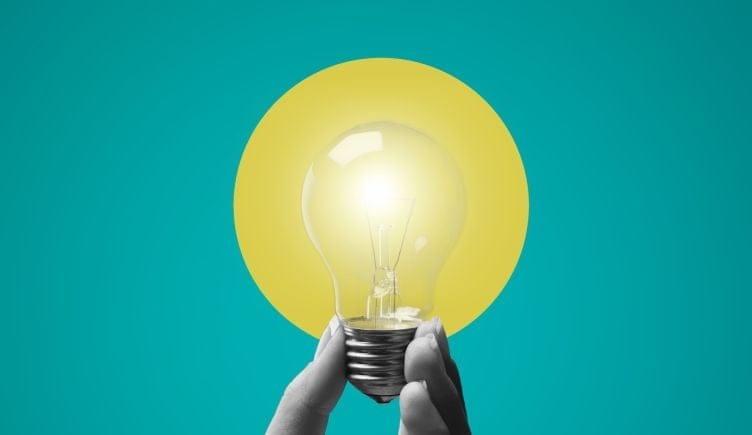 A hand holding a lit light bulb against a blue and yellow background