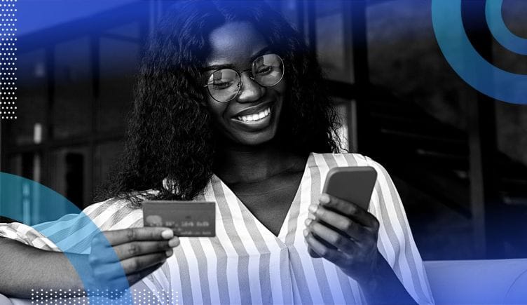 A smiling woman holding and looking at a smart phone and a credit card.