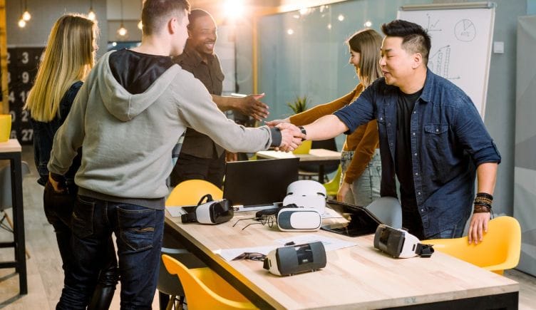 People shaking hands over a table with gaming consoles on them