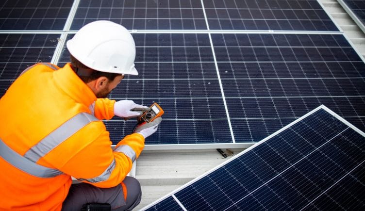 A man in a white hard hat and orange vest working on a solar panel.