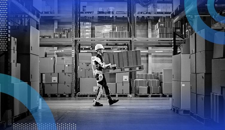 A man in a warehouse wearing a hardhat and robotic gear, which is helping him carry boxes.