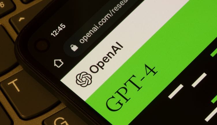A close-up photograph of OpenAI's GPT-4 displayed on a smartphone, and the smartphone is laying on a laptop keyboard