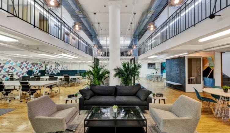 A large two-story open-floor-plan office space with tables for collaboration and a lounge area reminiscent of a home's living room.
