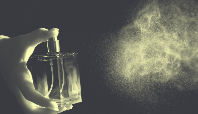 A hand sprays a bottle of perfume
